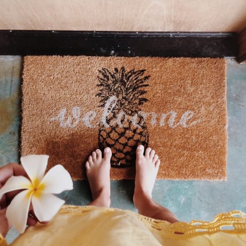 Woman standing on the door mat with a welcome writing holding frangipani flower in her hand